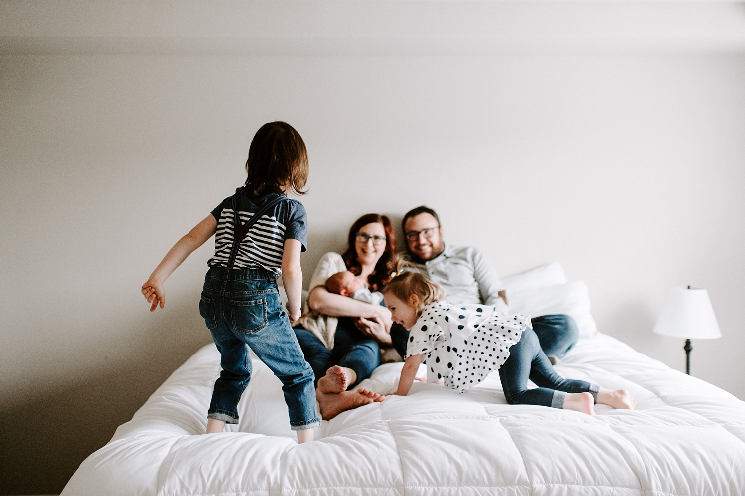 Toddlers jump on bed around parents and new baby during lifestyle photoshoot with Newborn Photographer, Meg Newton Photography
