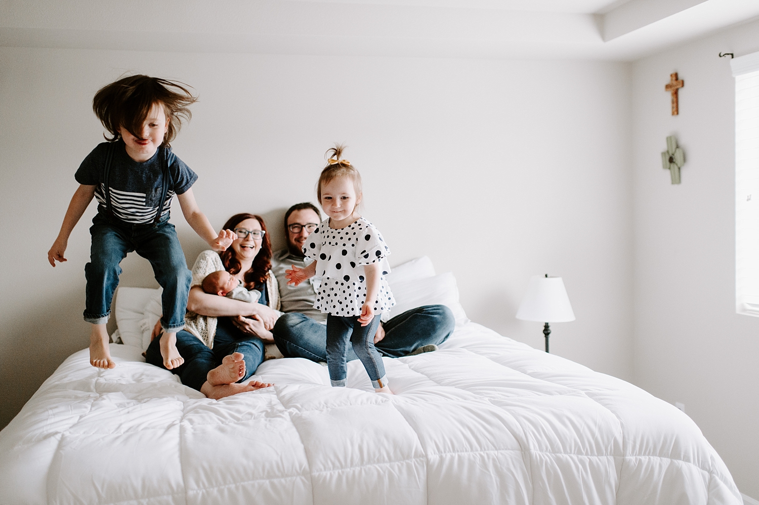 Toddlers jump on bed around parents and new baby during lifestyle photoshoot with Newborn Photographer, Meg Newton Photography