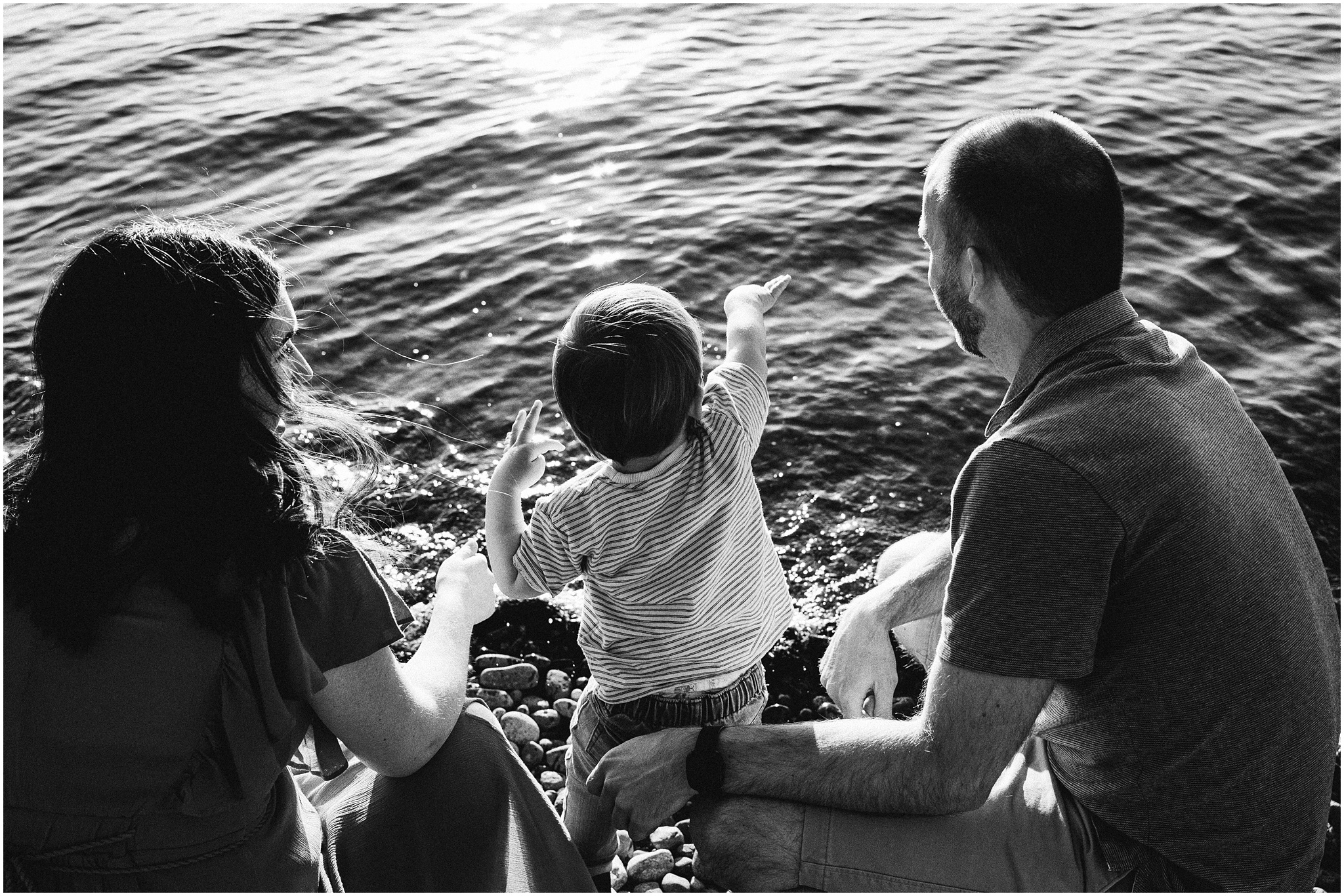 Little boy throws rocks into the lake while standing with his mom and dad. Photo by Meg Newton Photography.