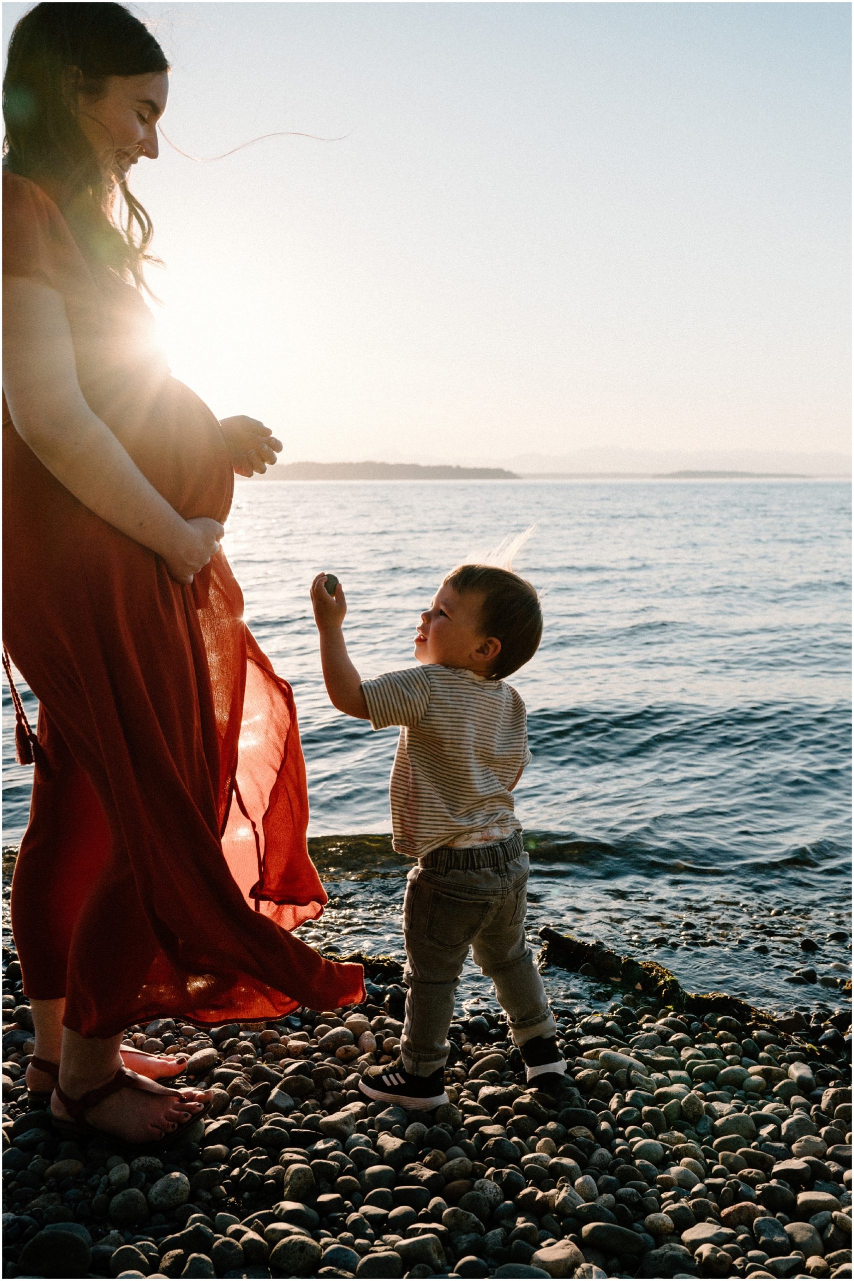 Little boy hands his mom a rock to skip on the lake. Photo by Meg Newton Photography.