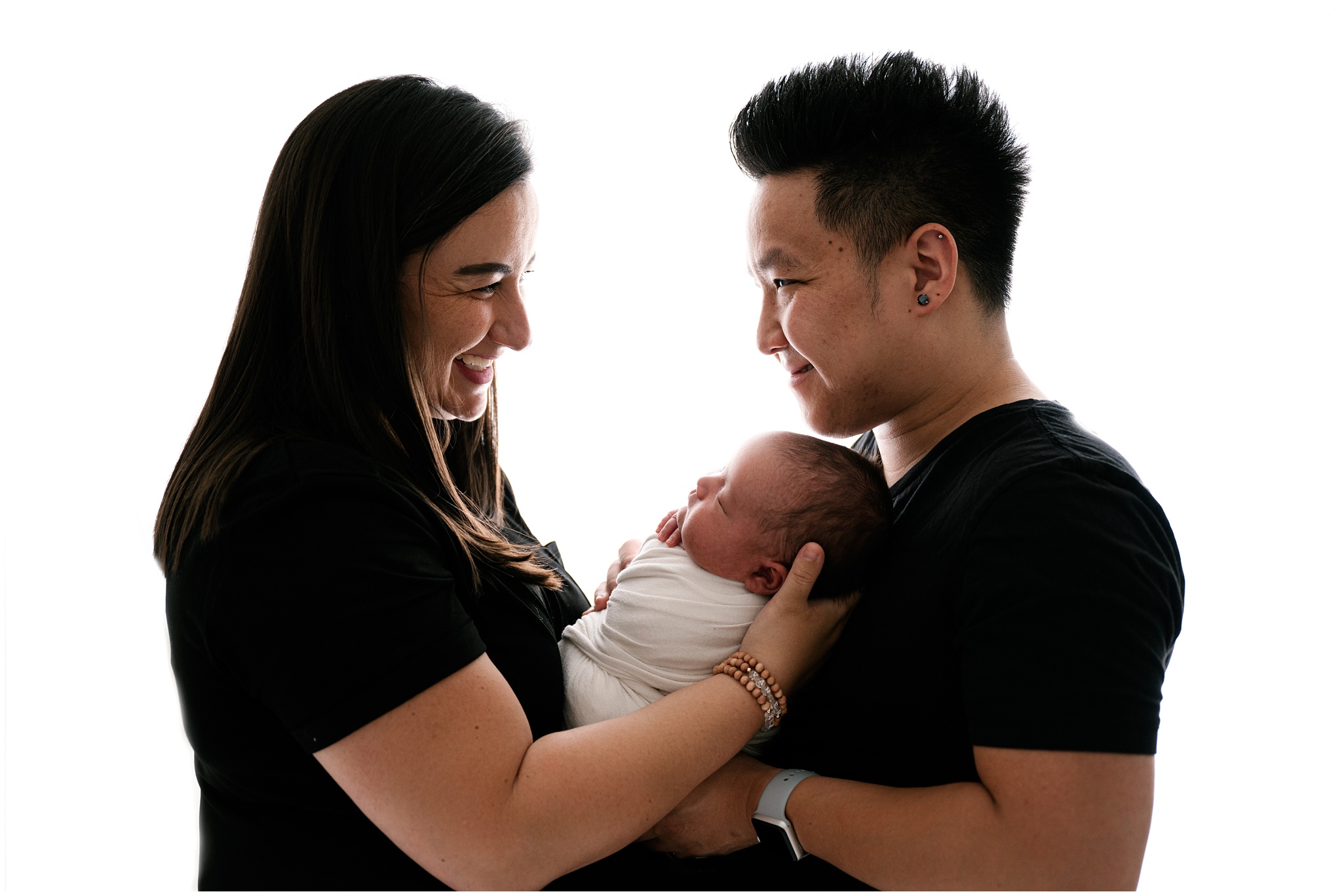 Mom and dad smile at one another while holding newborn son. Photo by Meg Newton Photography.