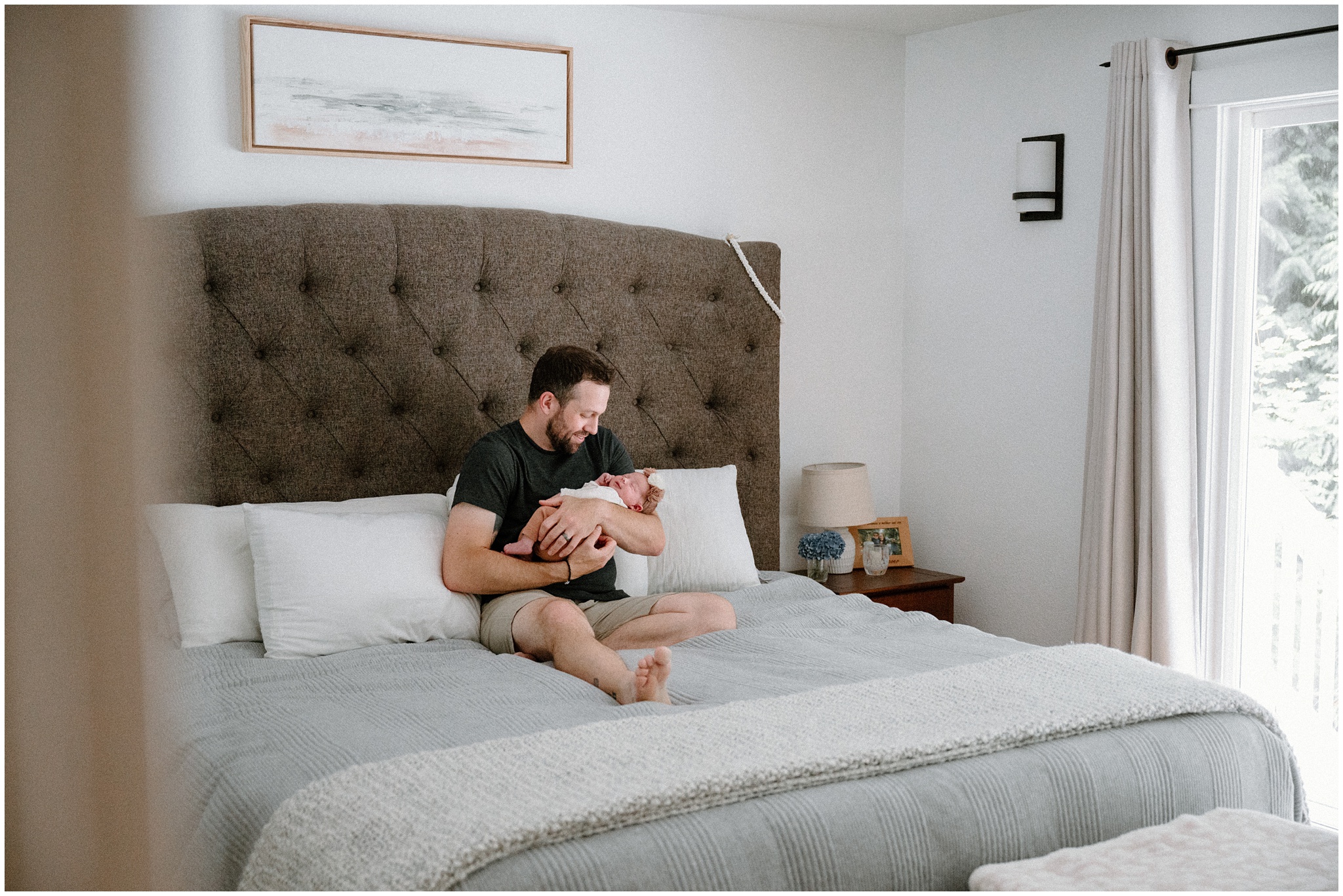 Dad snuggles with newborn daughter on bed. Photo by Meg Newton Photography.