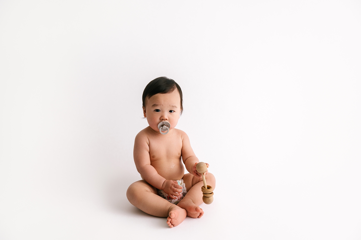 Baby boy holds rattle during sitter session. Photo by Meg Newton Photography.