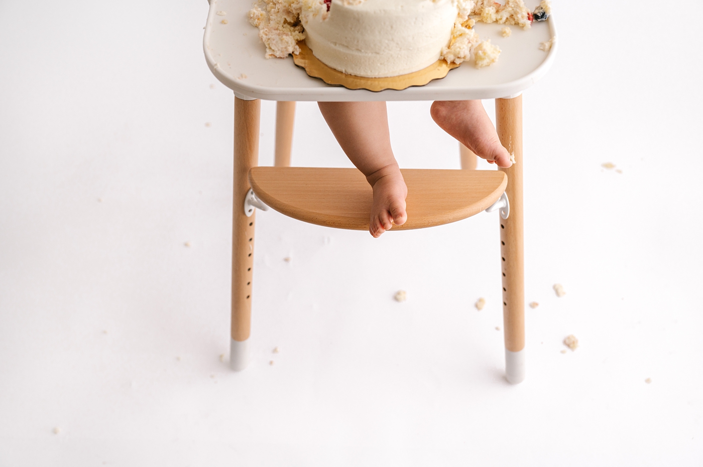 Little foot resting on highchair while crumbs are scattered on the floor. Photo by Meg Newton Photography.