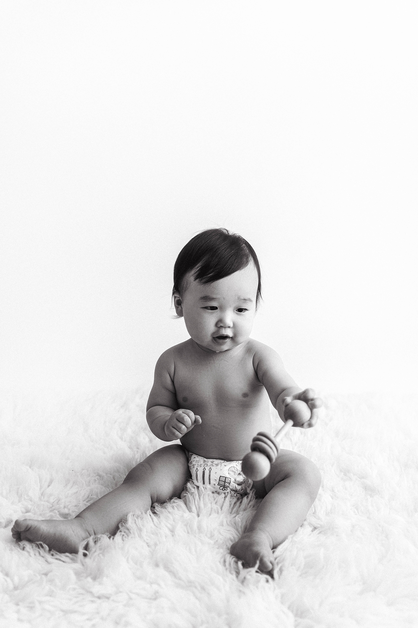 Baby boy playing with wooden rattle. Photo by Meg Newton Photography.
