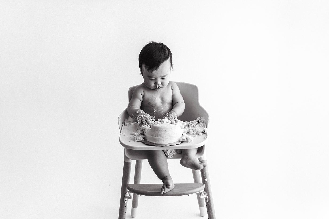 Baby boy smashes into cake while sitting in his highchair. Photo by Meg Newton Photography.