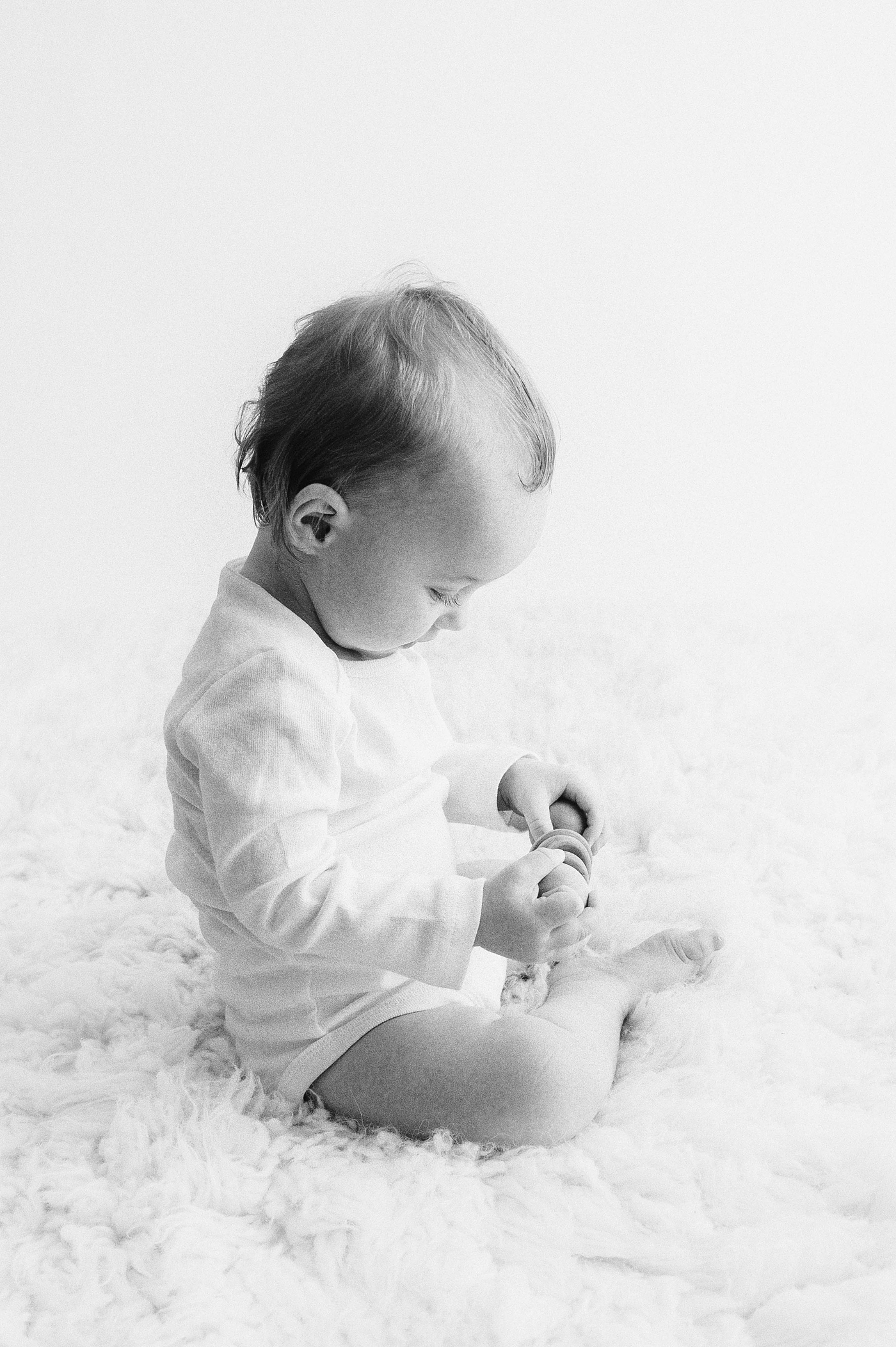 Baby boy studies wooden toy during one year old milestone session. Photo by Meg Newton Photography.