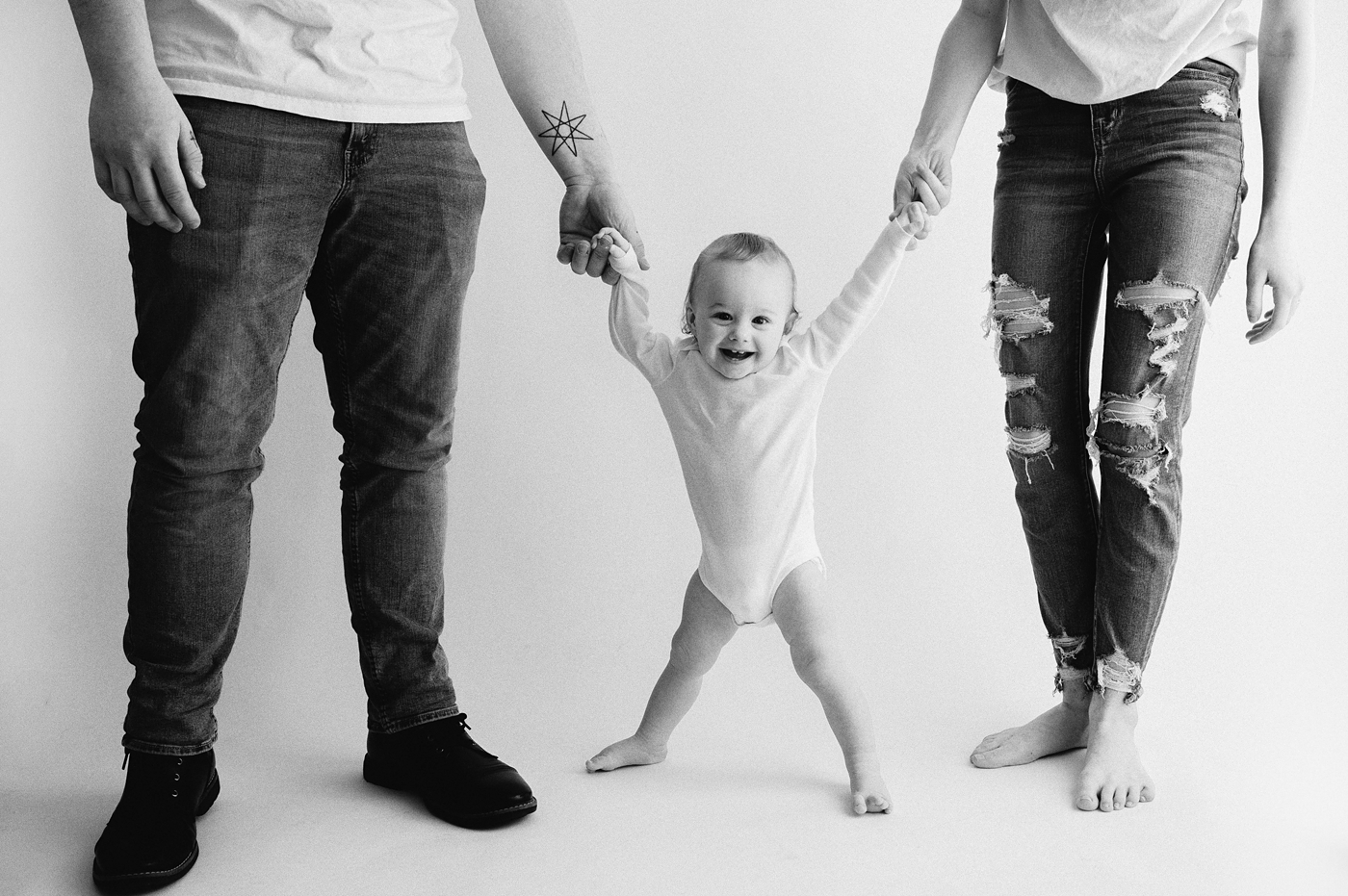 Black and white image of baby boy holding mom and dad's hands during Seattle milestone session. Photo by Meg Newton Photography.