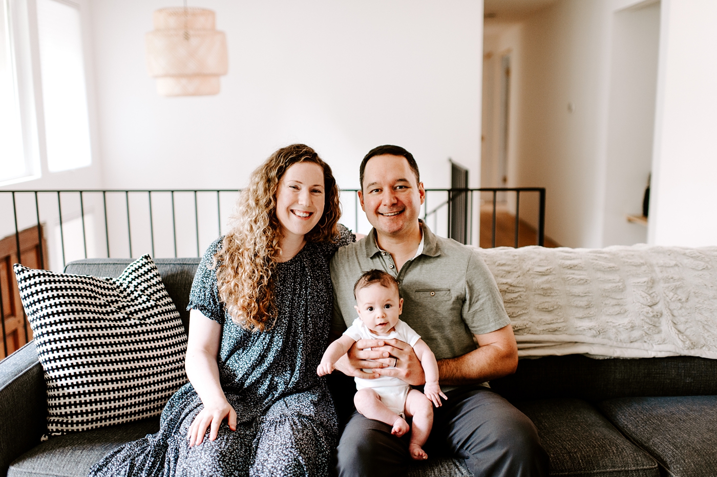 Proud parents hold son on grey couch. Photo by Meg Newton Photography.