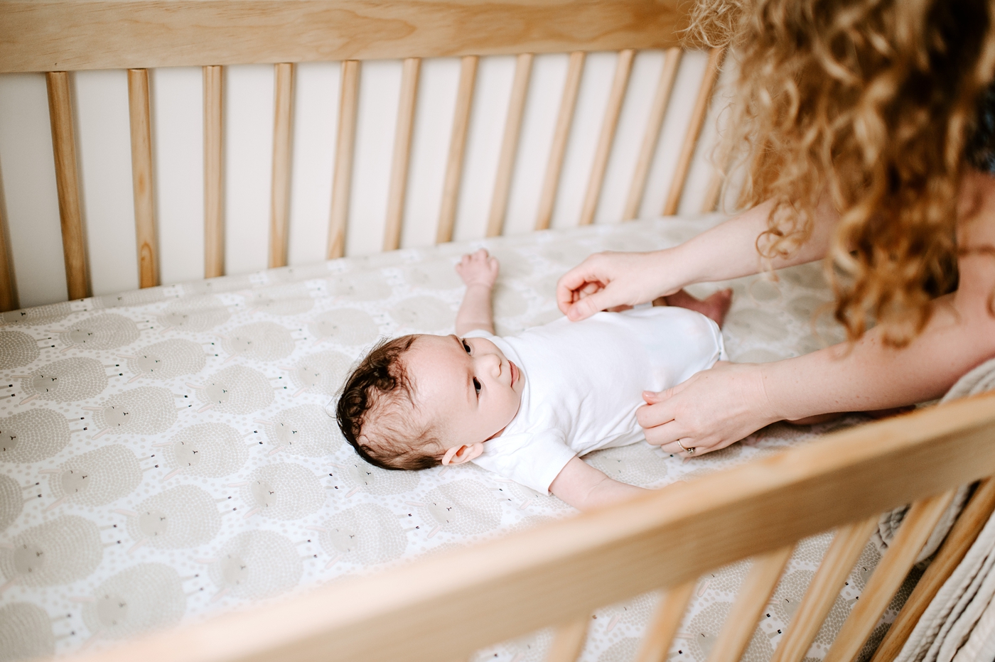 Mom tickles baby boy laying in his crib. Photo by Meg Newton Photography.