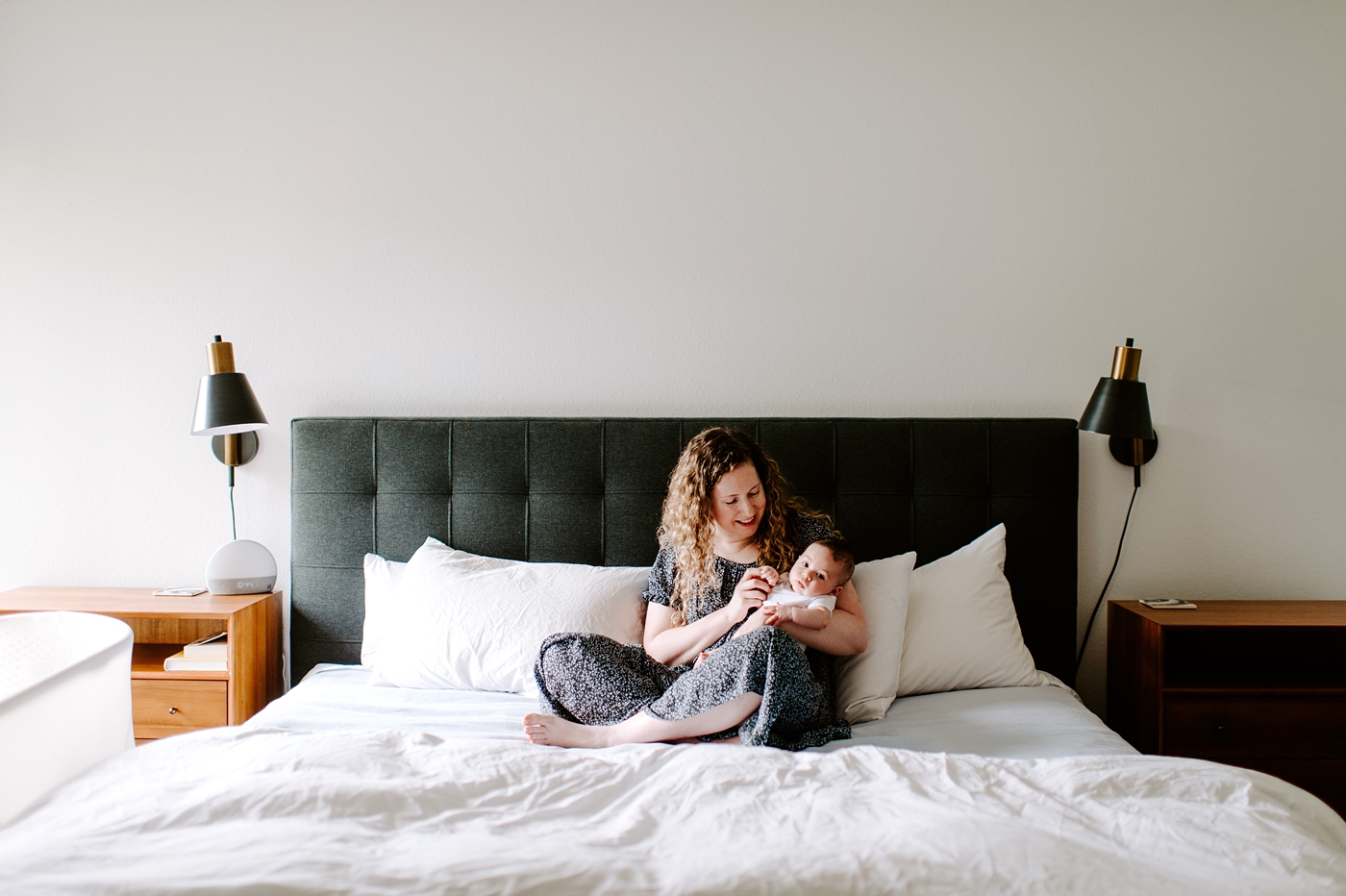 New mom holds son while sitting on bed during Seattle newborn session. Photo by Meg Newton Photography.