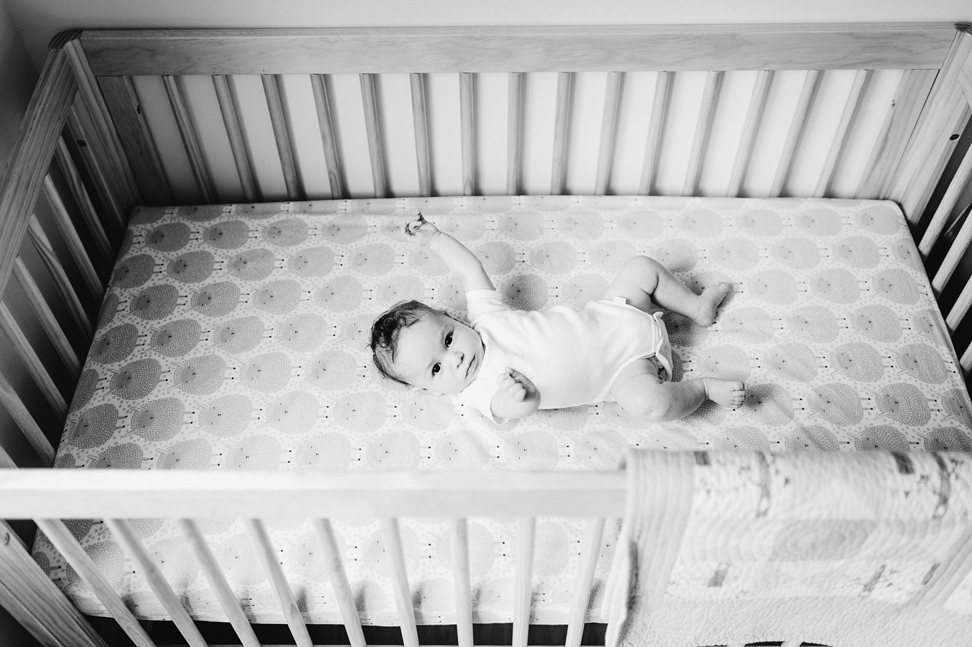 Baby boy kicks and moves arms while laying in crib. Photo by Meg Newton Photography.