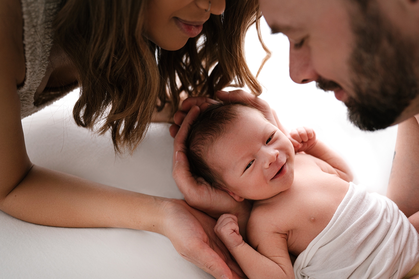 Newborn baby boy smiles while being cradled by his parents. Photo by Meg Newton Photography.