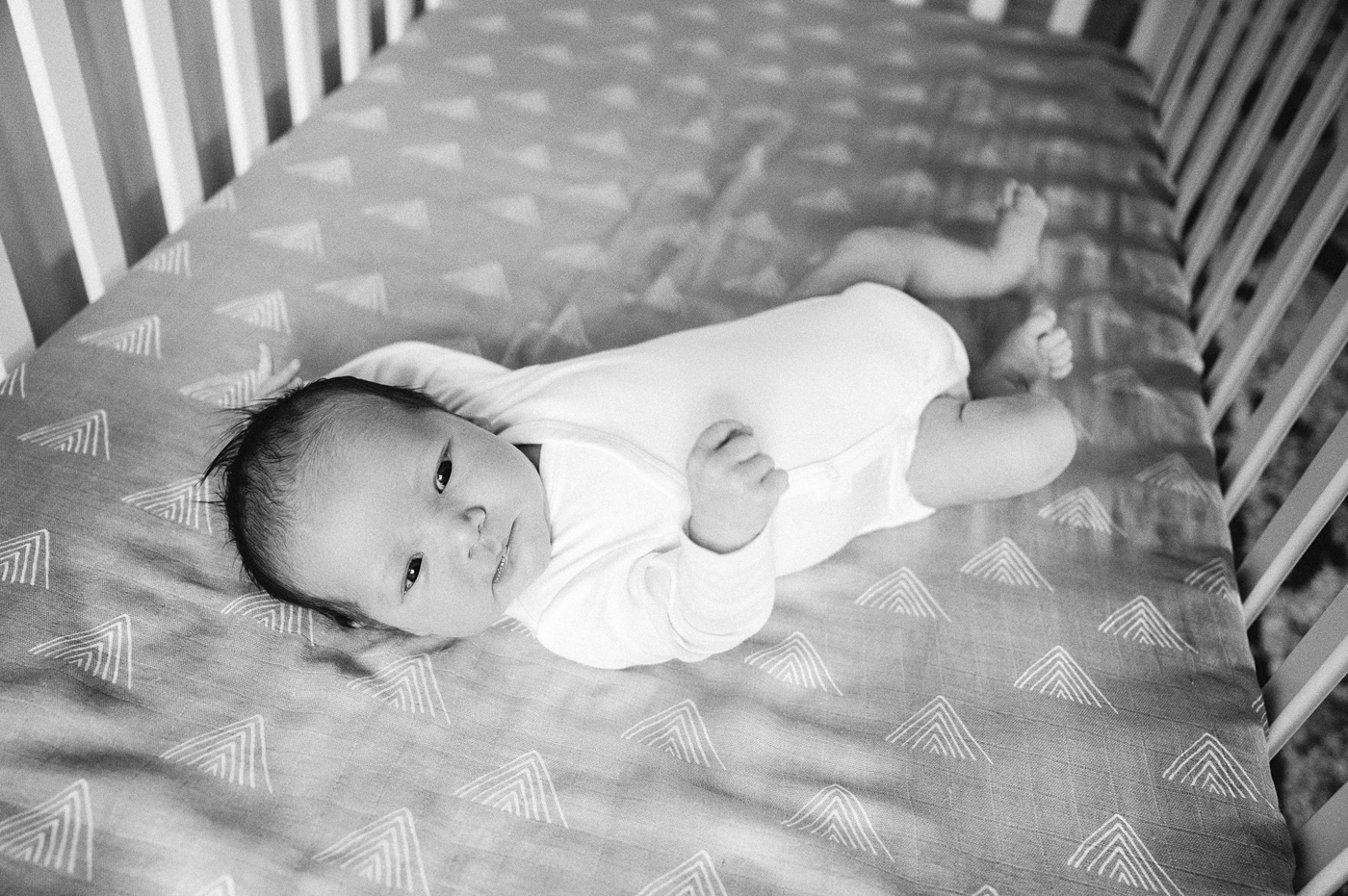 Black & White image of baby boy laying in crib during in home newborn session. Photo by Meg Newton Photography.