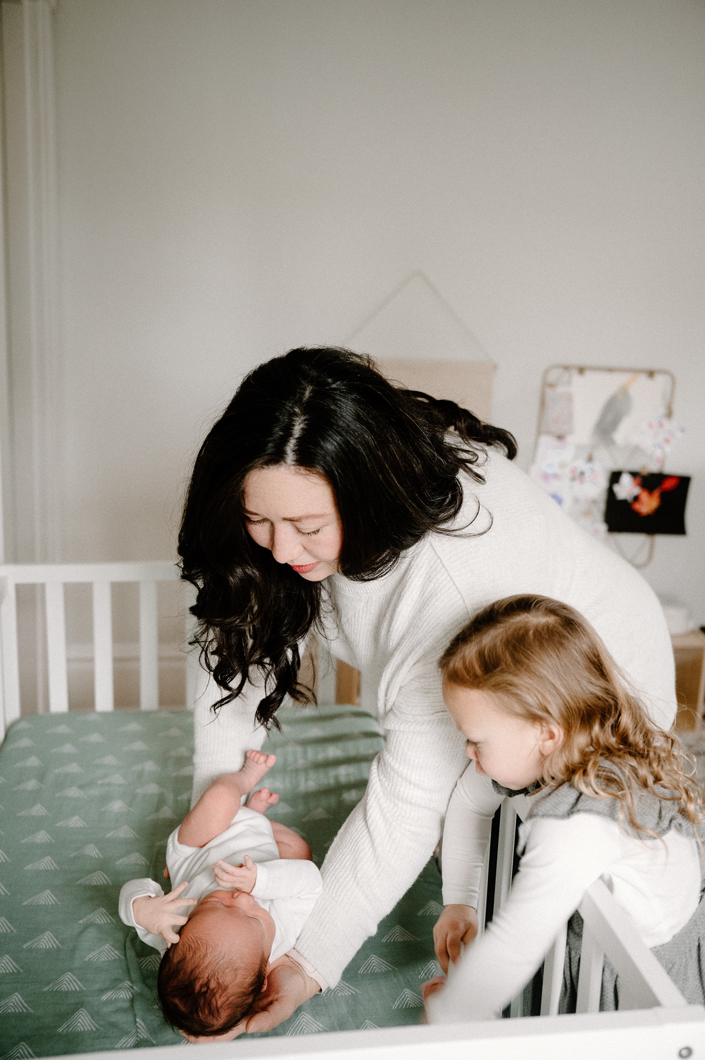 Mom lays baby in crib with big sister next to her during lifestyle in home newborn session. Photo by Meg Newton Photography.