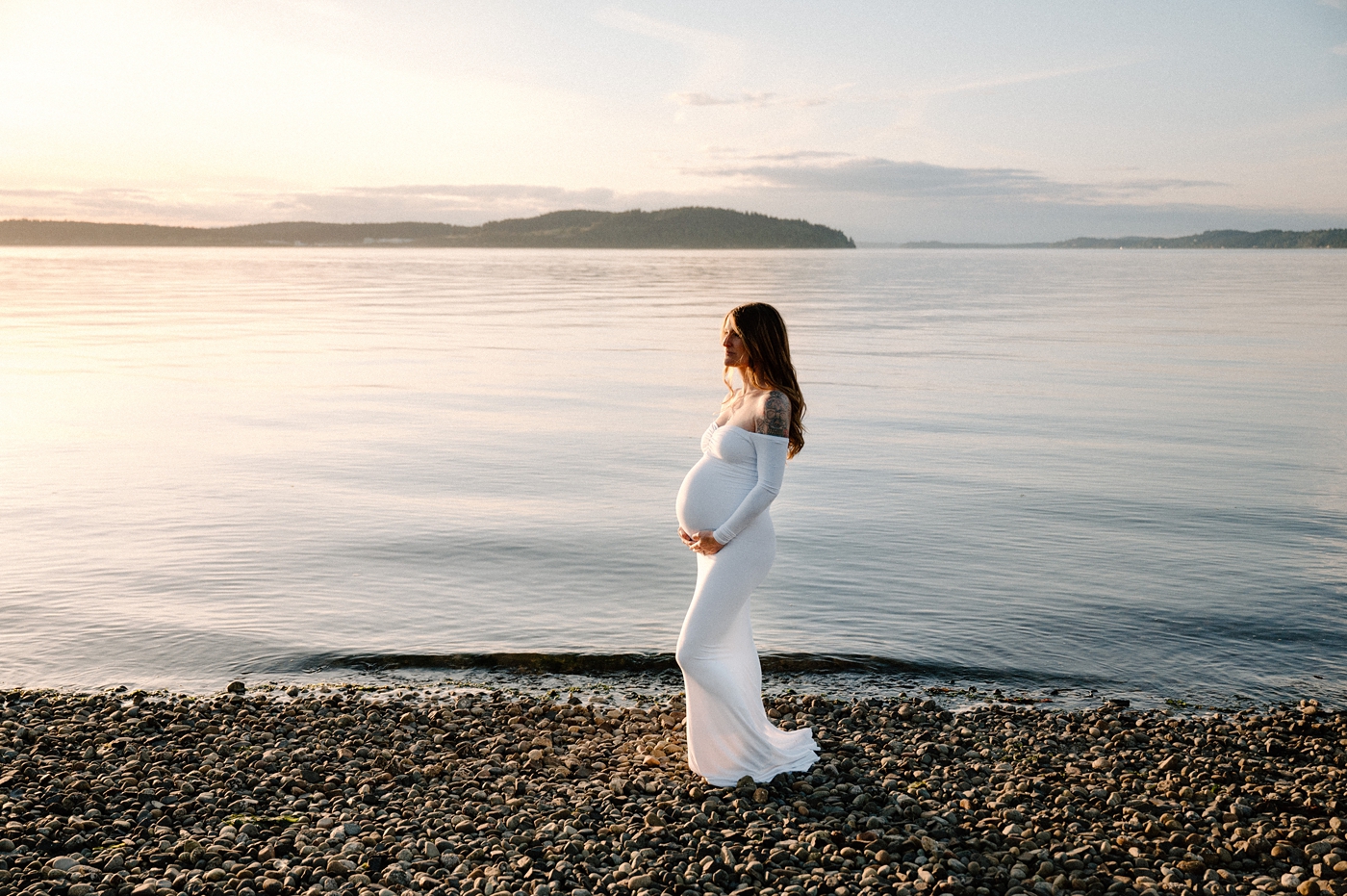 The water behind a new mom to be is still and glowing during her Washington maternity session. Image by PNW maternity photographer Meg Newton.