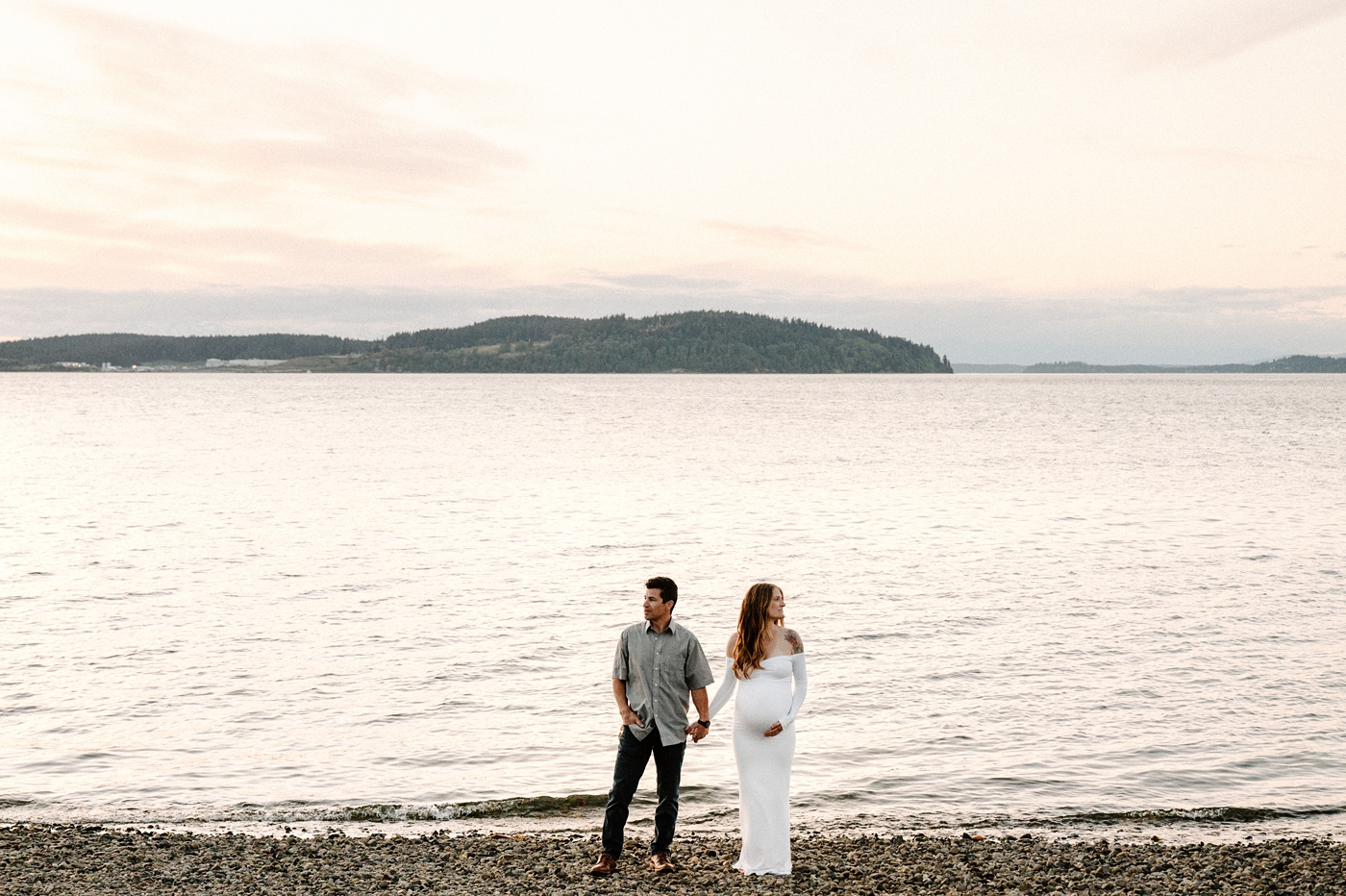 Parents to be look opposite directions in front of Hood Canal. Image by PNW maternity photographer Meg Newton.