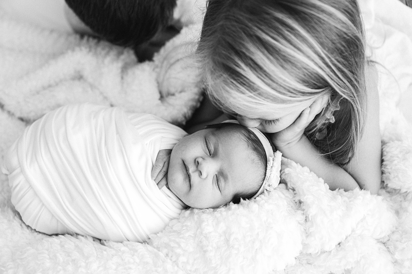 Big sister kisses newborn sister atop her head. Image by Meg Newton Photography.