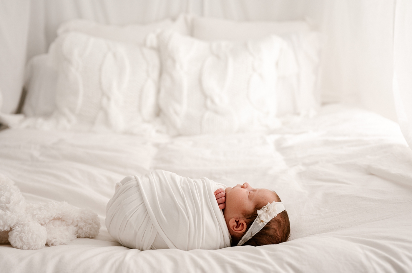 Baby girl lays on bed during lifestyle studio session. Image by Meg Newton Photography.