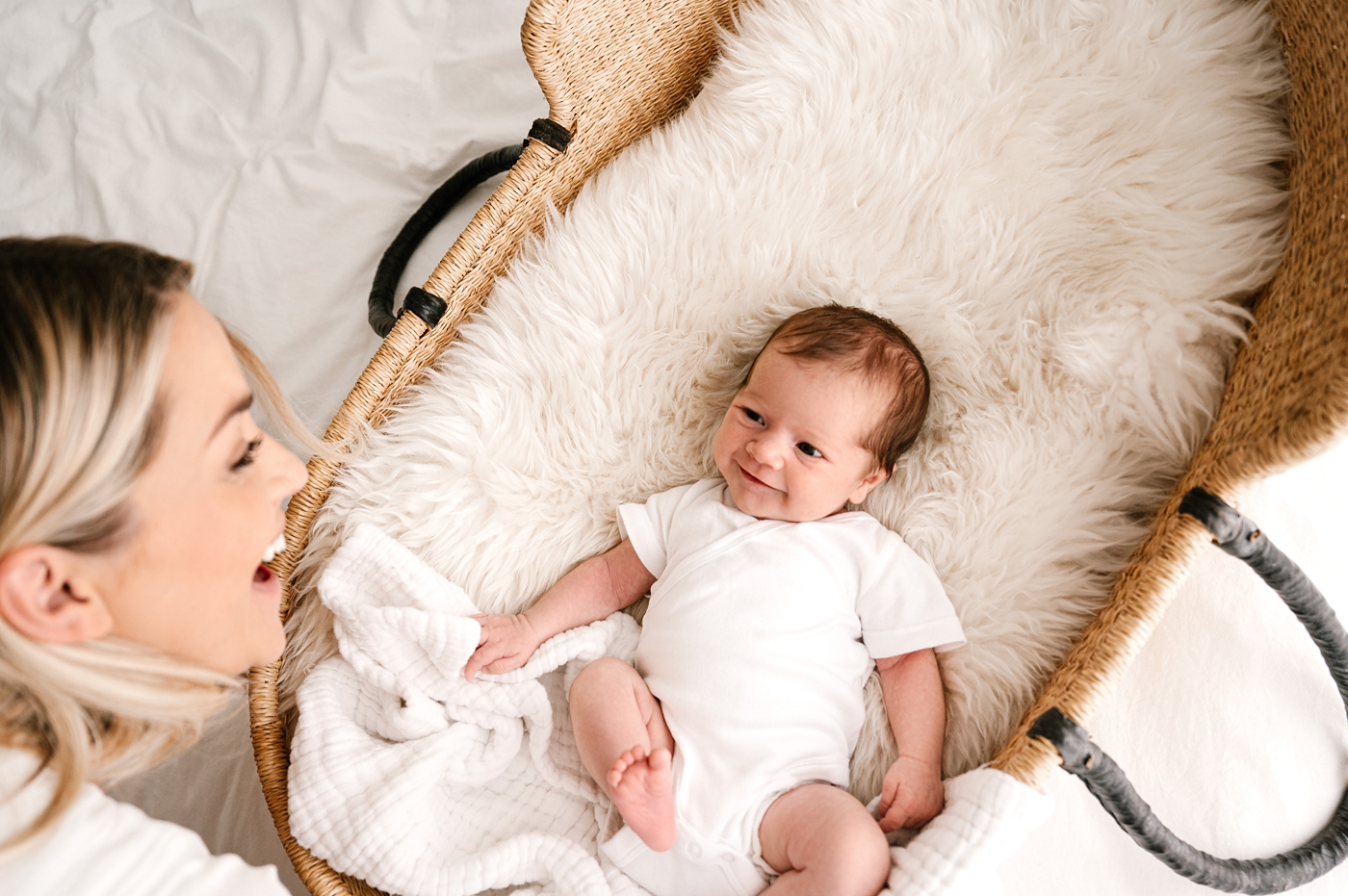 Mom and baby grin at one another while laying in bassinet. Image by Meg Newton Photography.