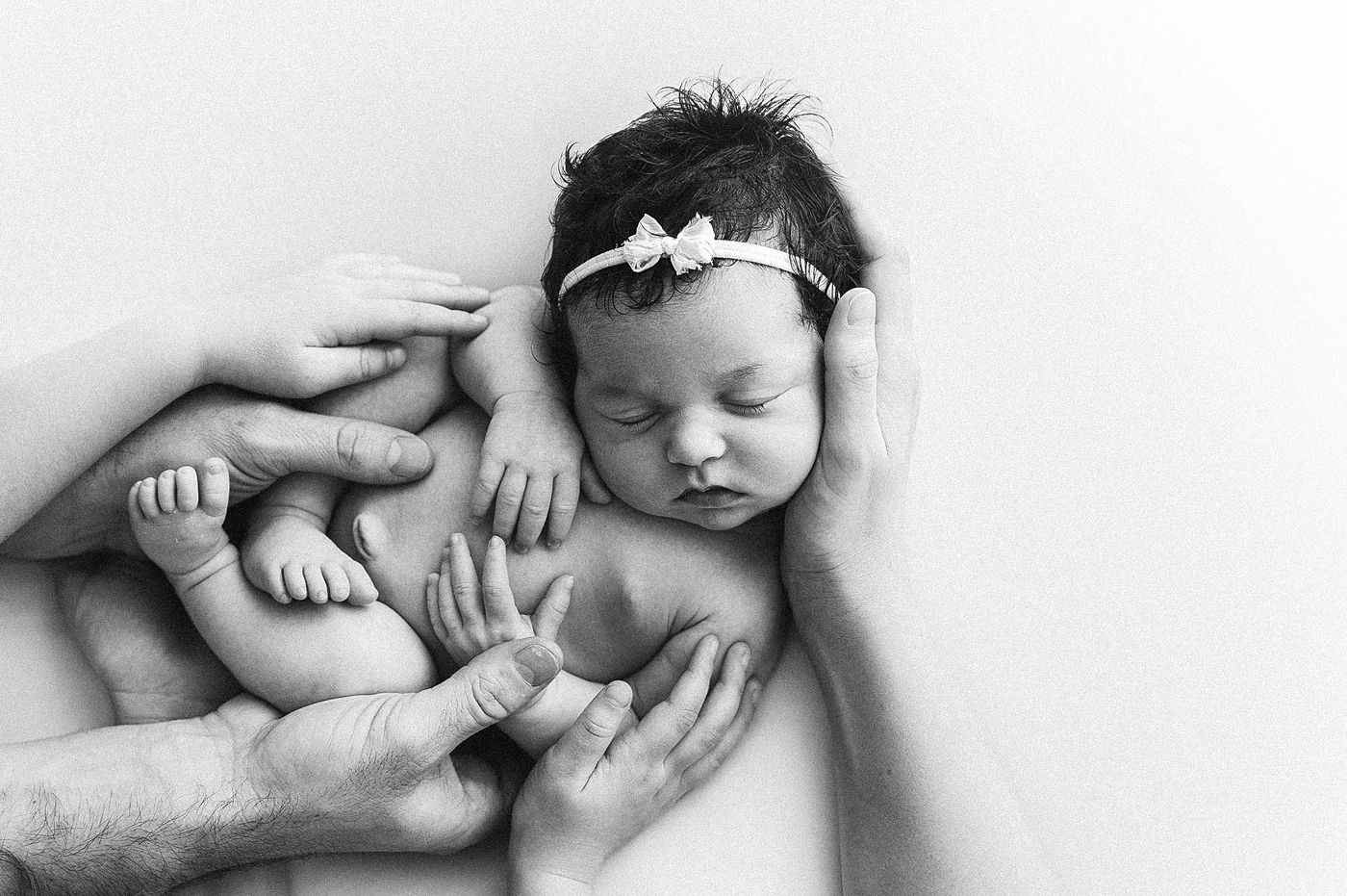 Hands of various family members lovingly embrace newborn child. Image by Meg Newton Photography.