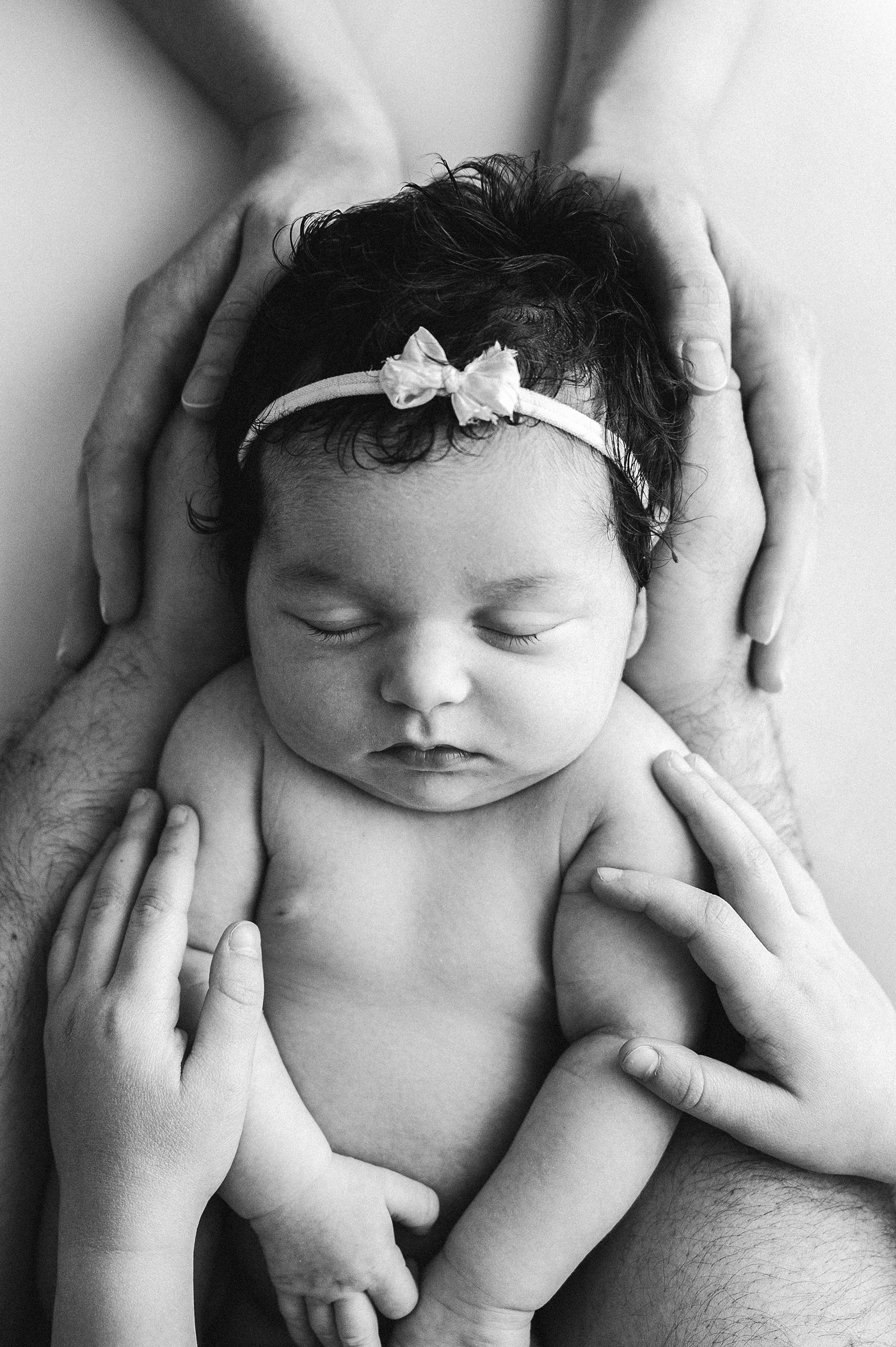 All the hands in the family hold newborn daughter. Image by Meg Newton Photography.