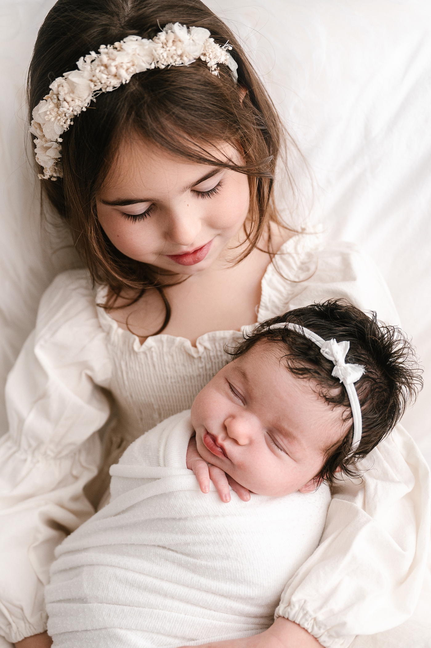 Baby sister sleeps in big sisters arms during studio newborn session. Image by Meg Newton Photography.