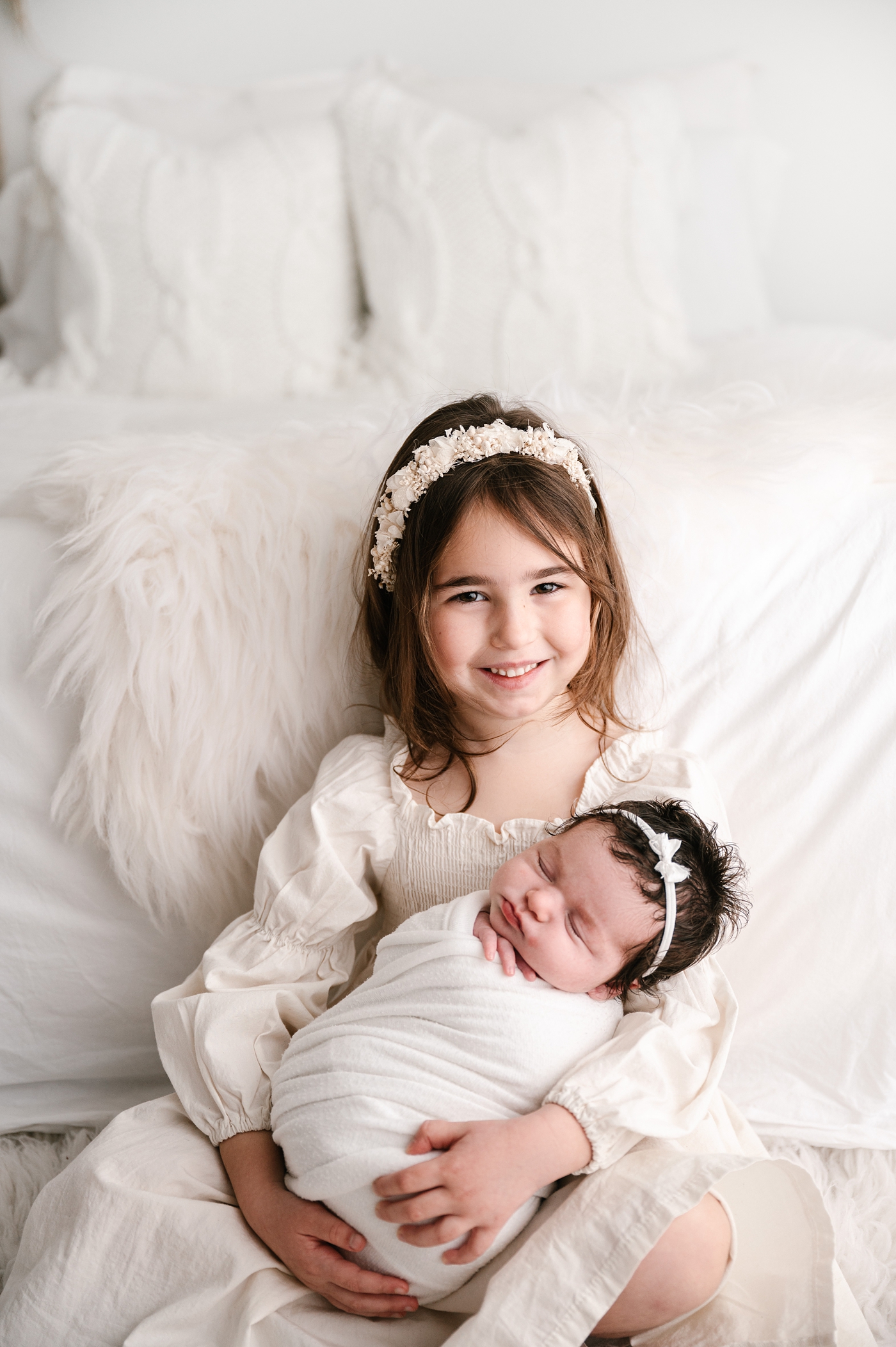 Proud big sister holds her newborn sister during studio newborn session. Image by Meg Newton Photography.