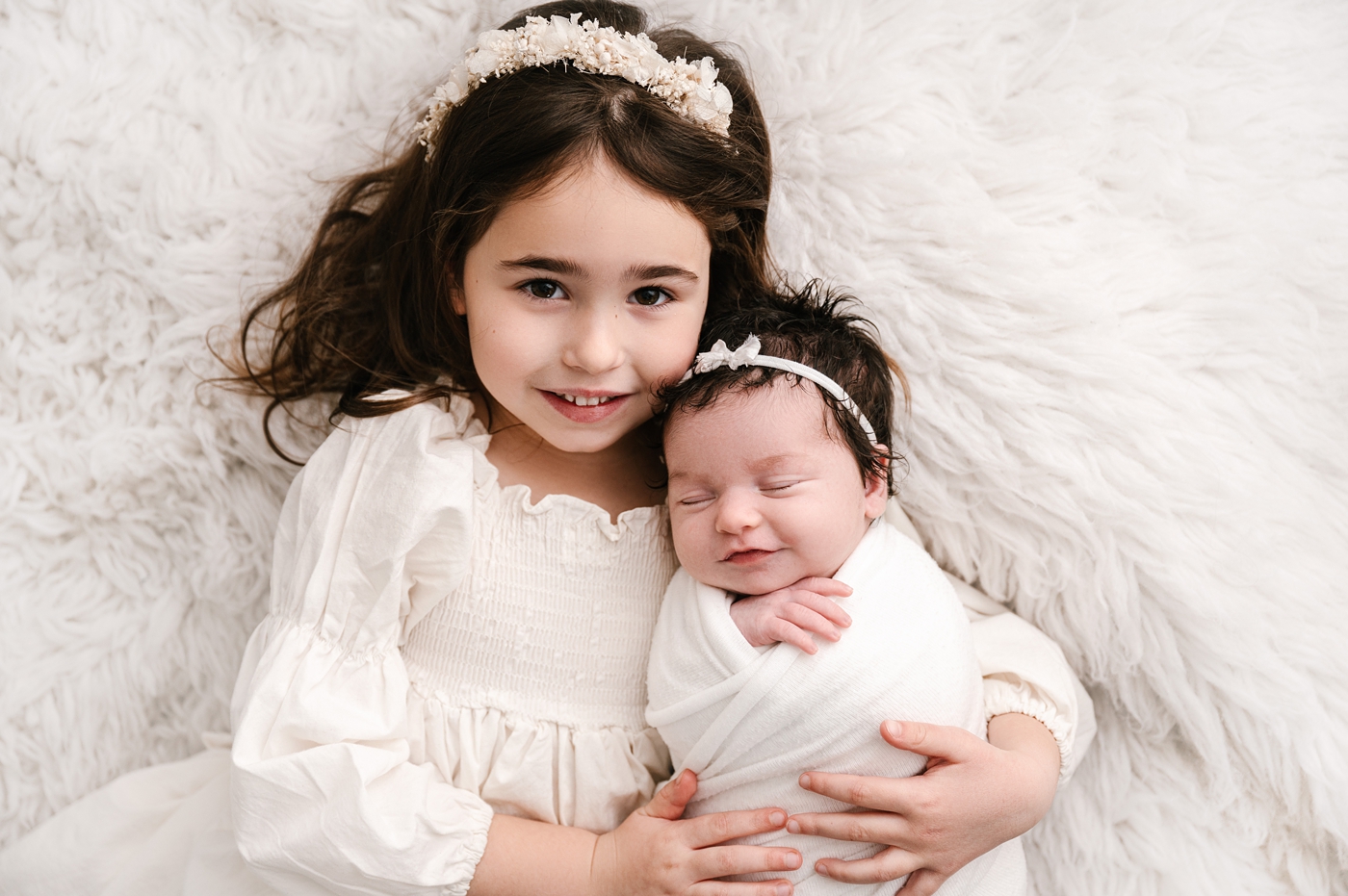 Big sister holds newborn baby sister during Tacoma newborn session. Image by Meg Newton Photography.