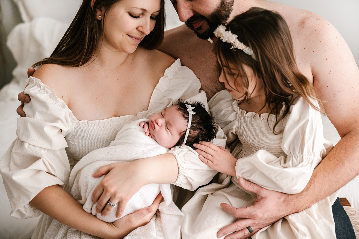 Family snuggles in and looks over newborn. Image by Meg Newton Photography.