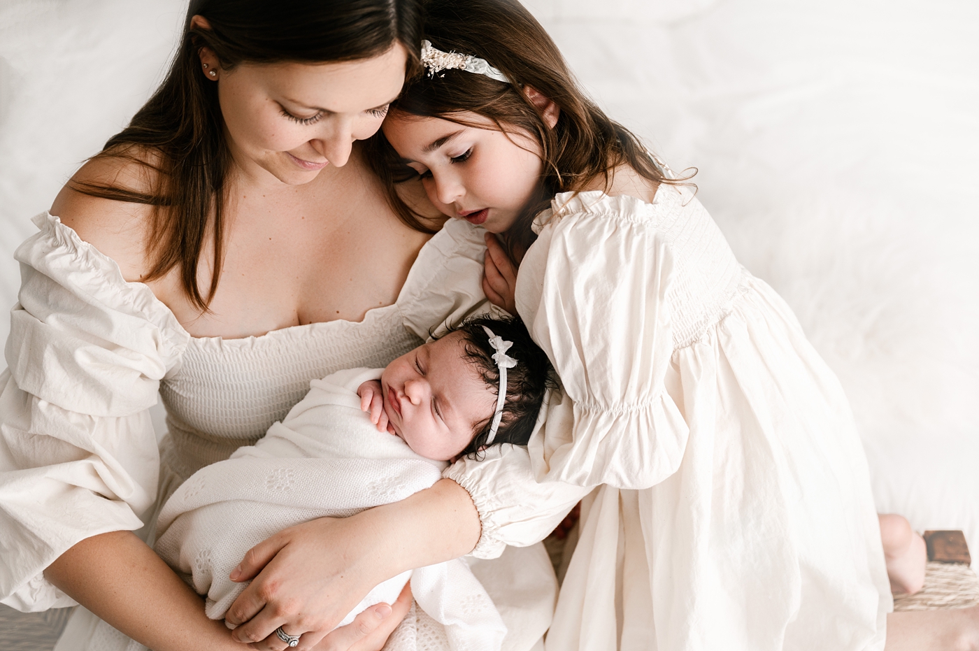 Mom and daughters snuggle during studio newborn session. Image by Meg Newton Photography.