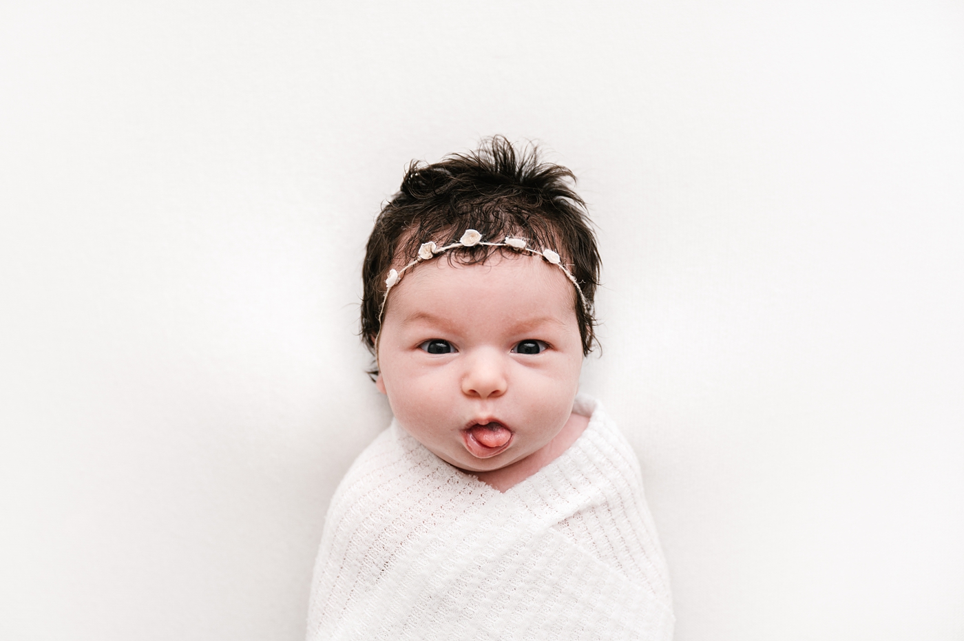 Baby girl sticks her tongue out during studio newborn session. Image by Meg Newton Photography.
