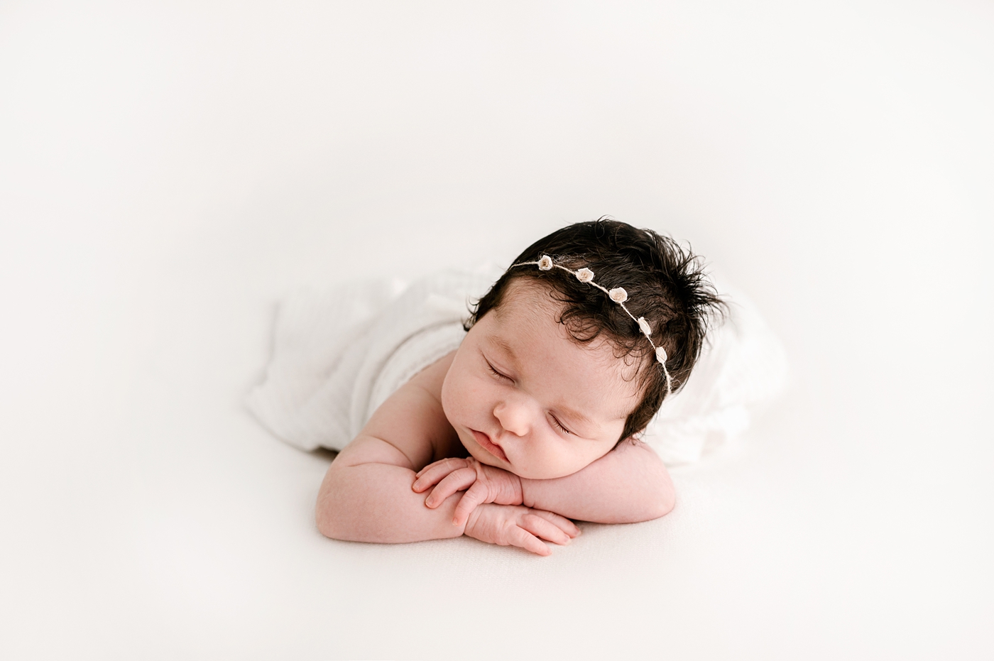 Baby girl poses with her head over her hands during studio newborn session. Image by Meg Newton Photography.