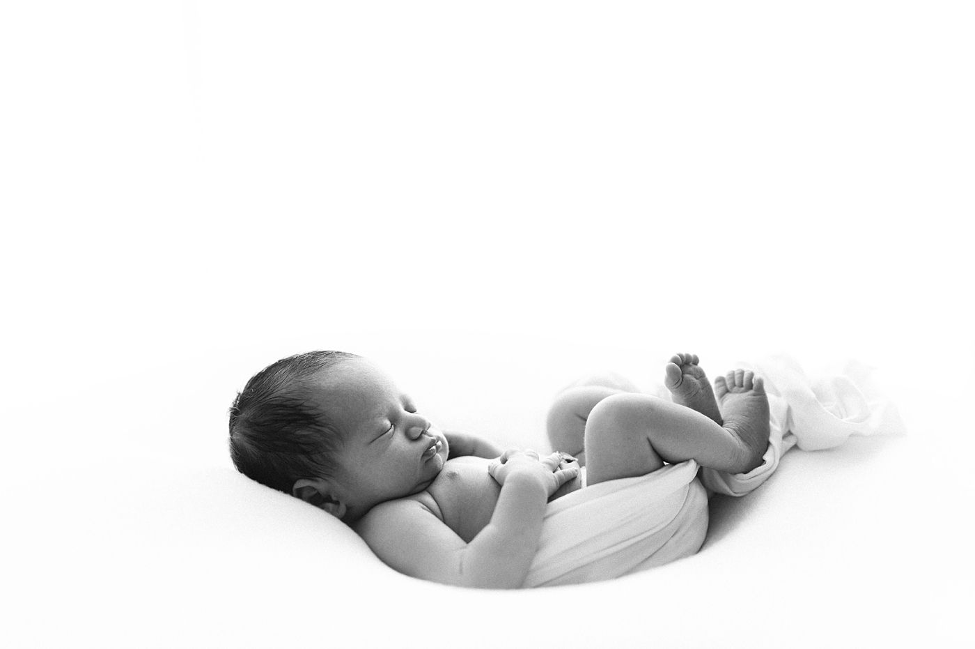 Black and white image of baby peacefully sleeping during his newborn session. Photo by Meg Newton Photography.