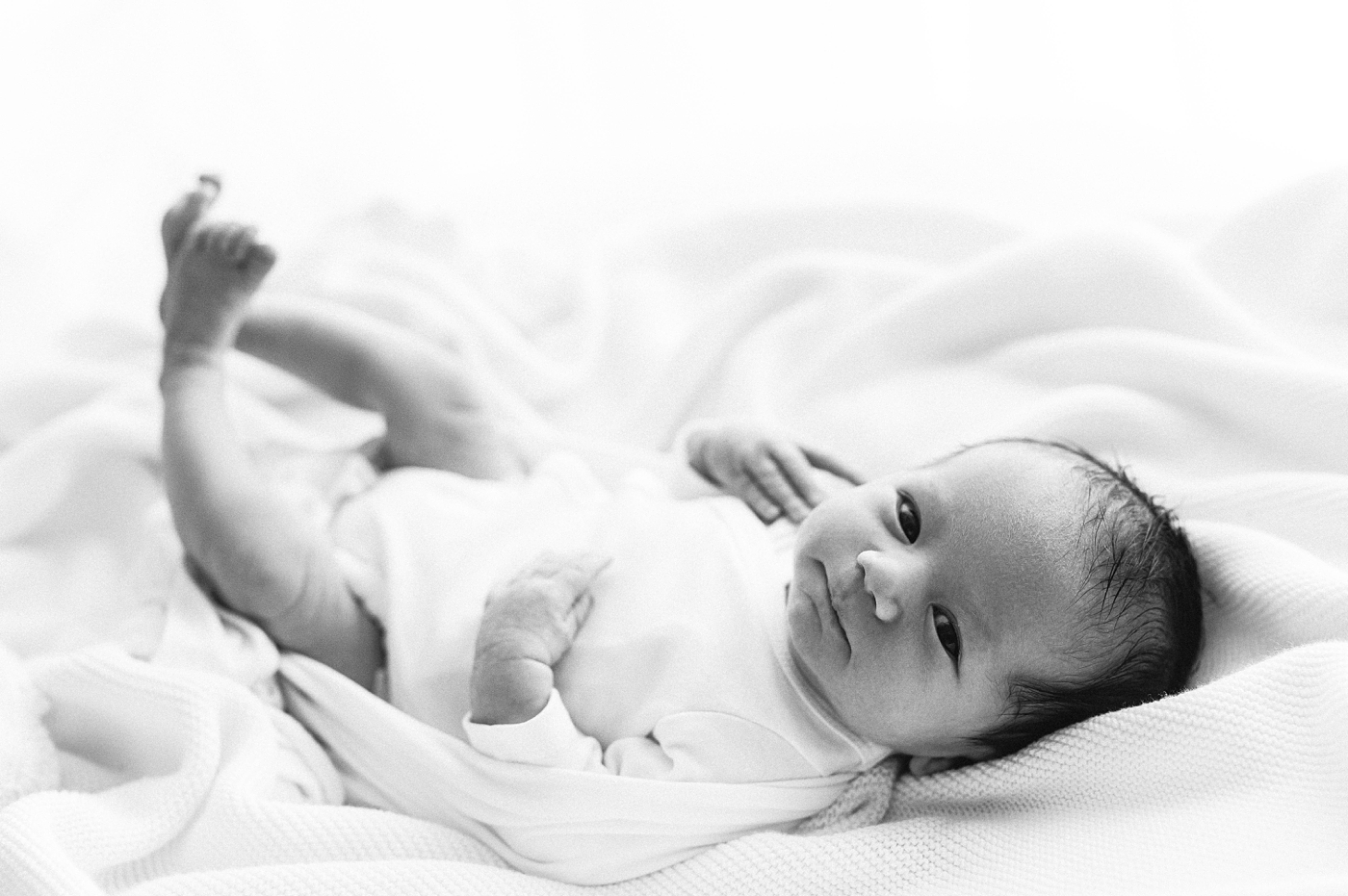 Baby boy lays on swaddle blankets in white onesie. Photo by Meg Newton Photography.
