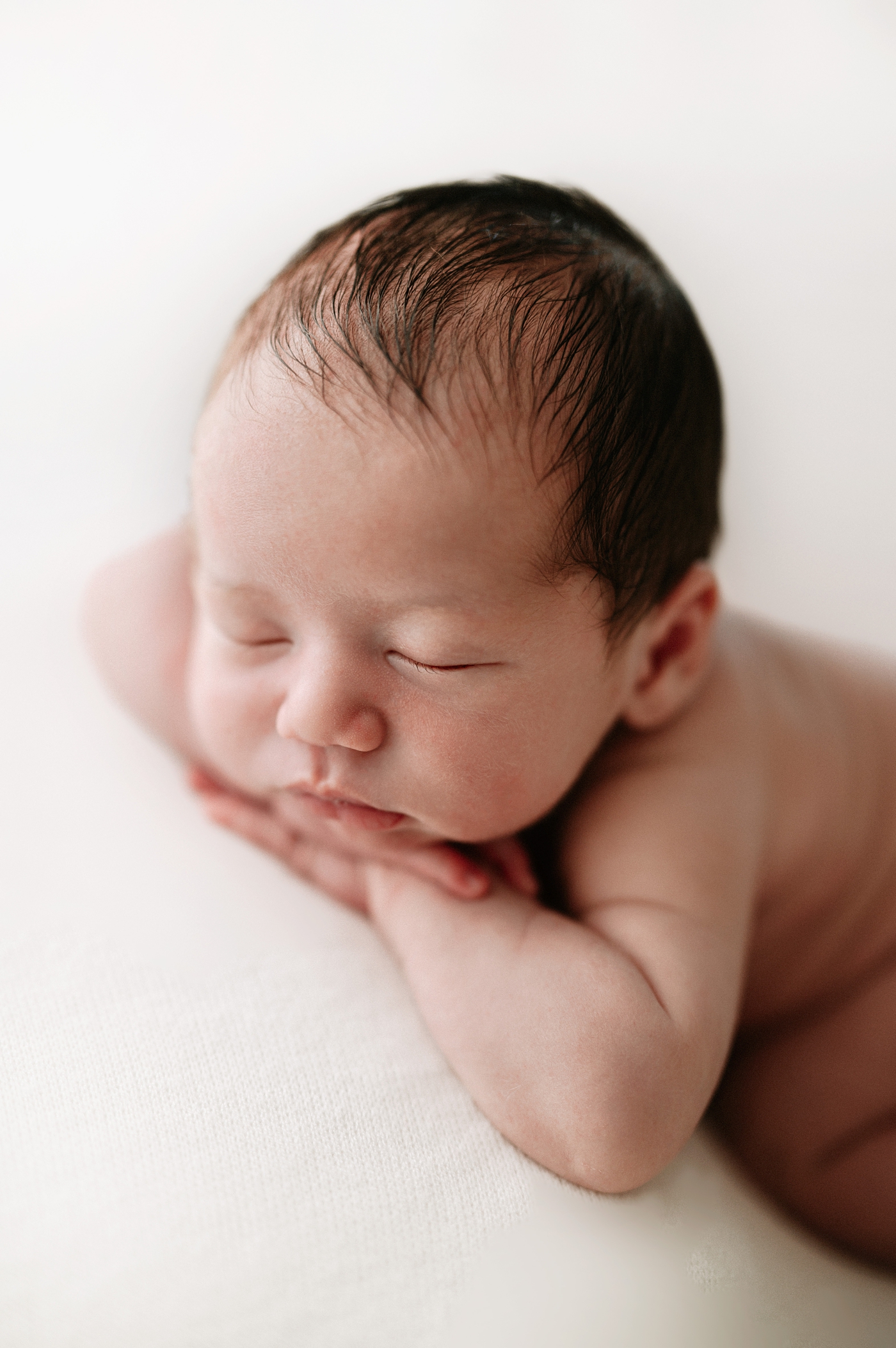 Baby lays with hands under chin. Photo by Meg Newton Photography.