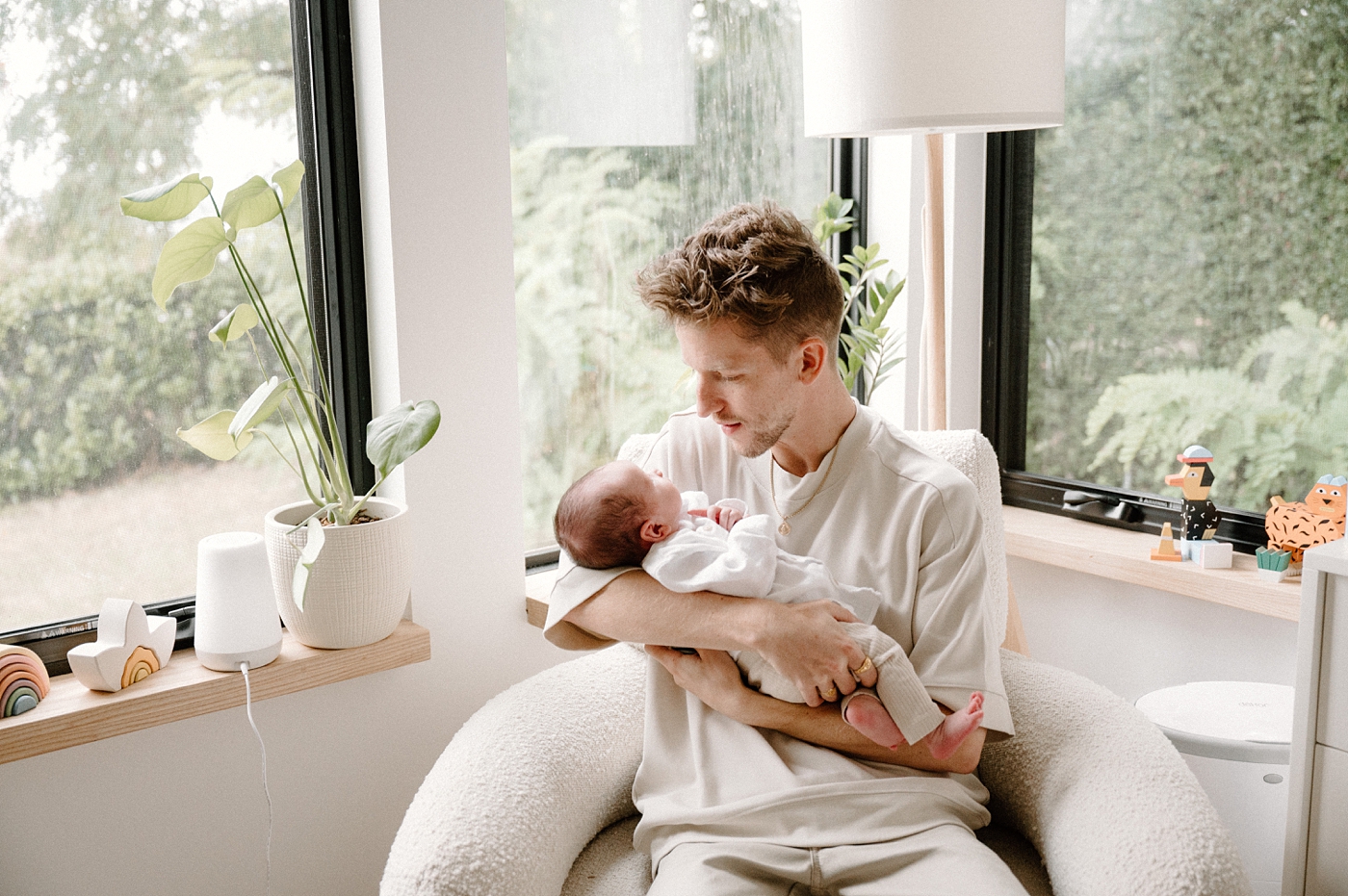 Dad holds baby boy in front of an array of windows. Photo by Meg Newton Photography.