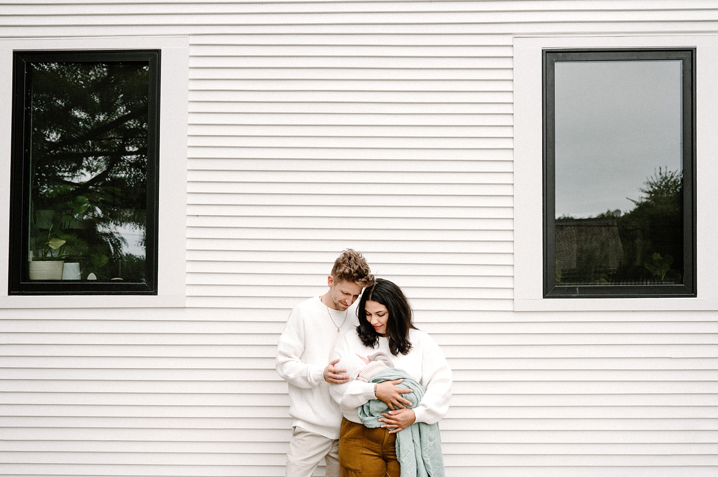 Mom and dad hold son while standing next to the siding on their house. Photo by Meg Newton Photography.