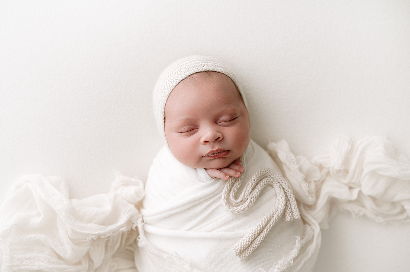 Baby boy in cream bonnet during studio newborn session. Photo by Meg Newton Photography.