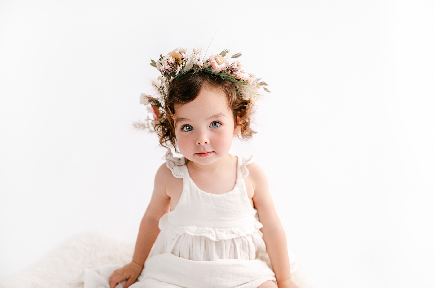 Baby girl in white dress wears floral crown. Photo by Meg Newton Photography.